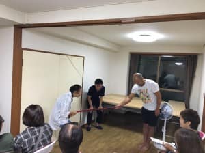 棒立ち右手だけの花本VS足を広げ、深く腰を落として、両手の女性ヘルパーの綱引き対決